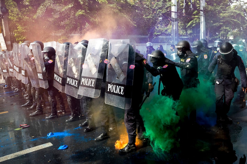 Riot police stand in formation as pro-democracy protesters throw smoke bombs near the Parliament in Bangkok