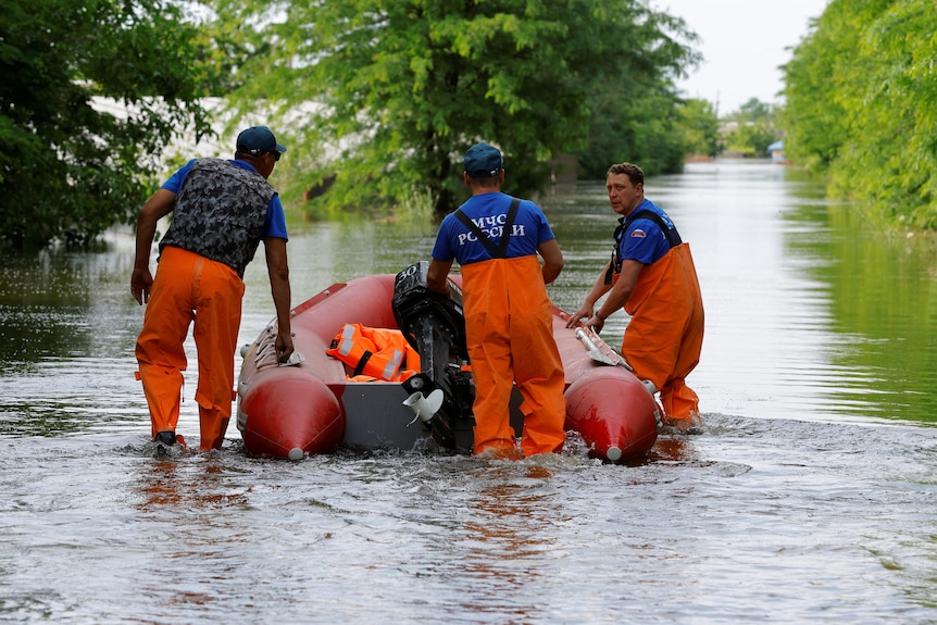 People stand beside a rubber boat in water that can be seen well into the distance.