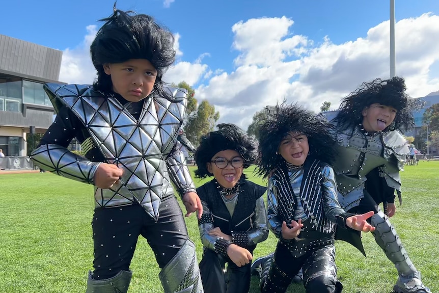 Four boys were black rock and roll star style wigs and KISS band costumes and pose as rock stars on a football field.