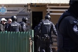 Police officers in tactical gear outside a property they raided.  