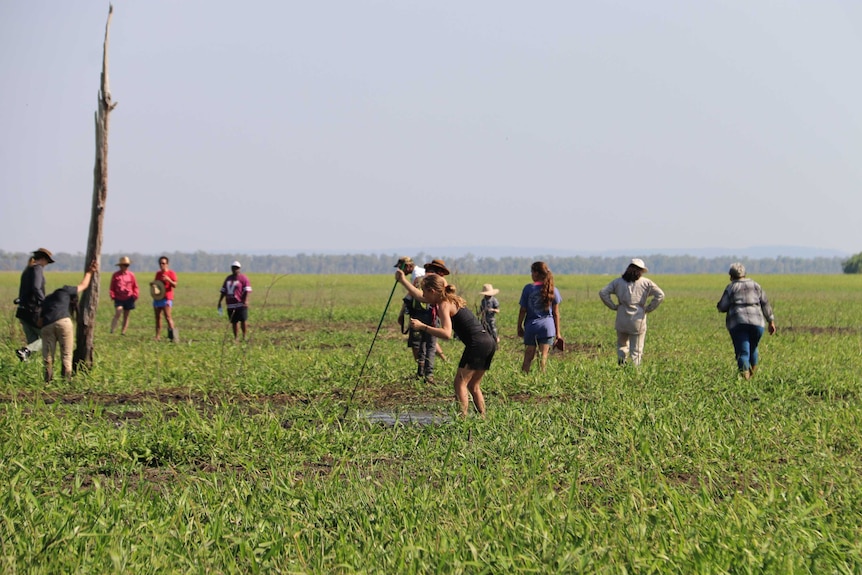 About 10 people walk through a green, muddy plain.