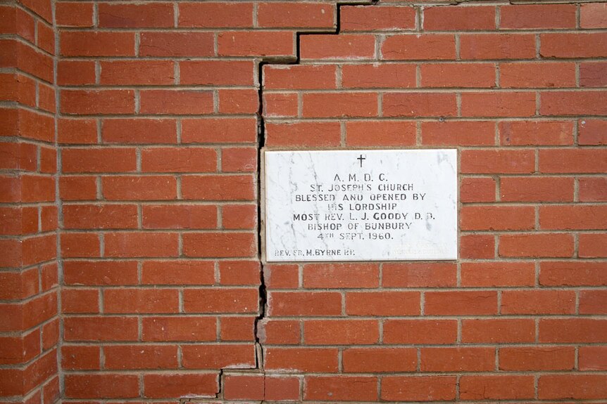 A crack in the red brick wall of a church near a marble plaque