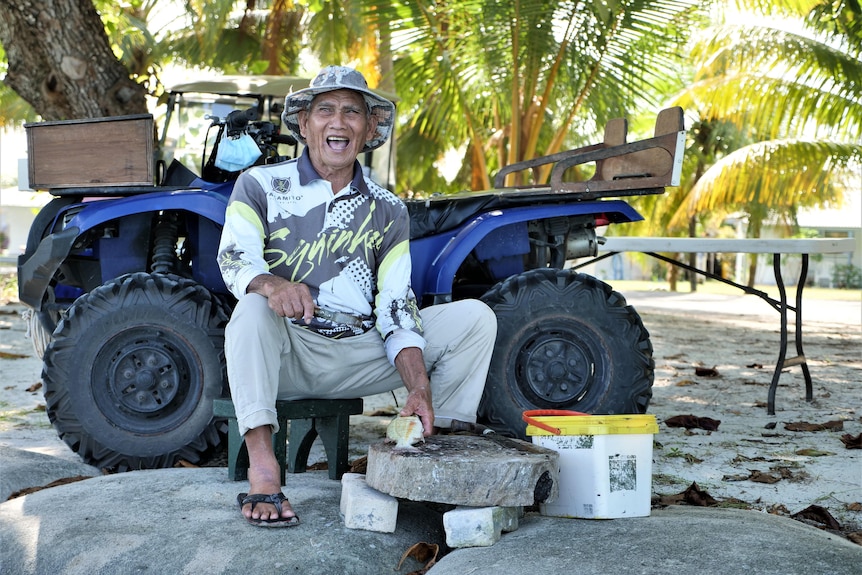 Man smiling at the camera with fish in hand and four wheeler behind.