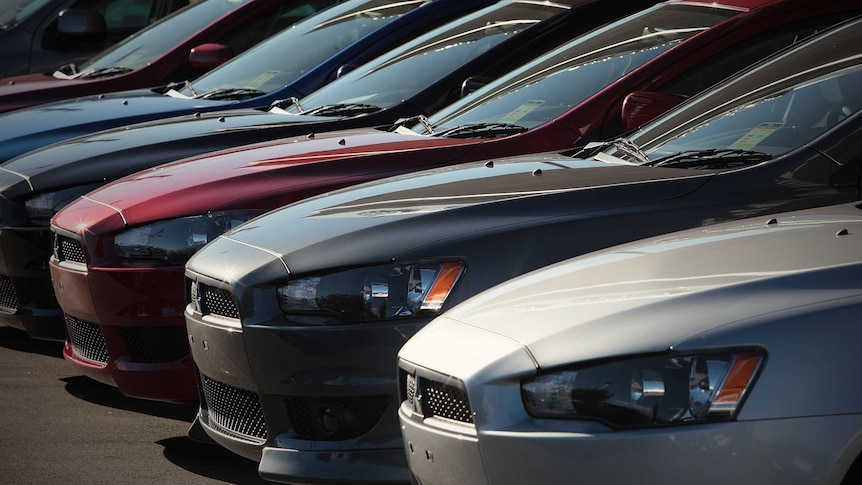 A row of cars sit at a vehicle dealership.