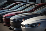 A row of new cars sit at a vehicle dealership.