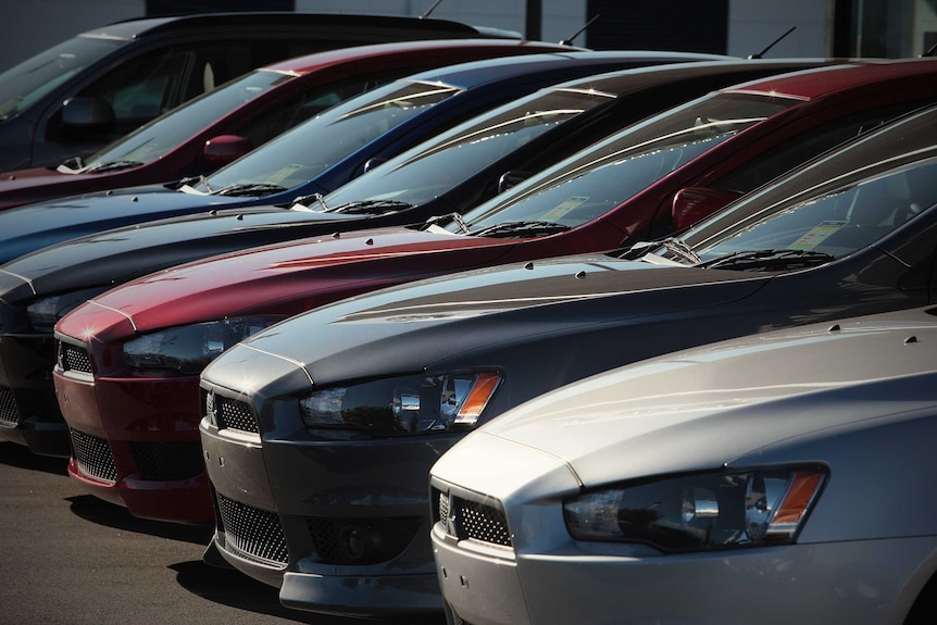 A row of cars sit at a vehicle dealership.