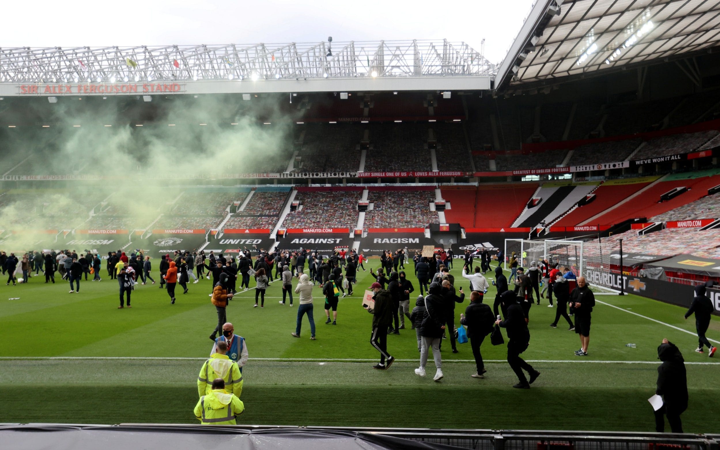 a crowd of people in plain clothes holding signs march onto the pitch at a football stadium 