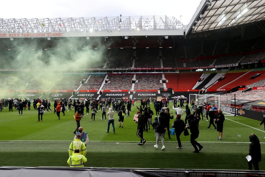 a crowd of people in plain clothes holding signs march onto the pitch at a football stadium 