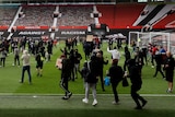 a crowd of people in plain clothes holding signs march onto the pitch at a football stadium 
