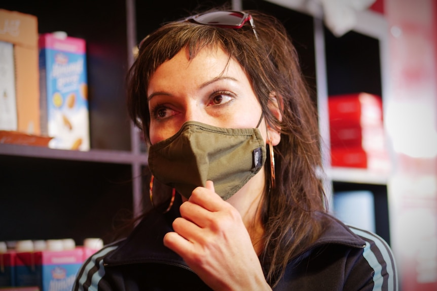 A woman with a green mask looks to the left of camera