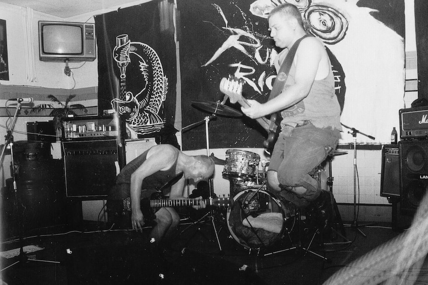 Black and white image of a punk band leaping and working a dingy pub stage