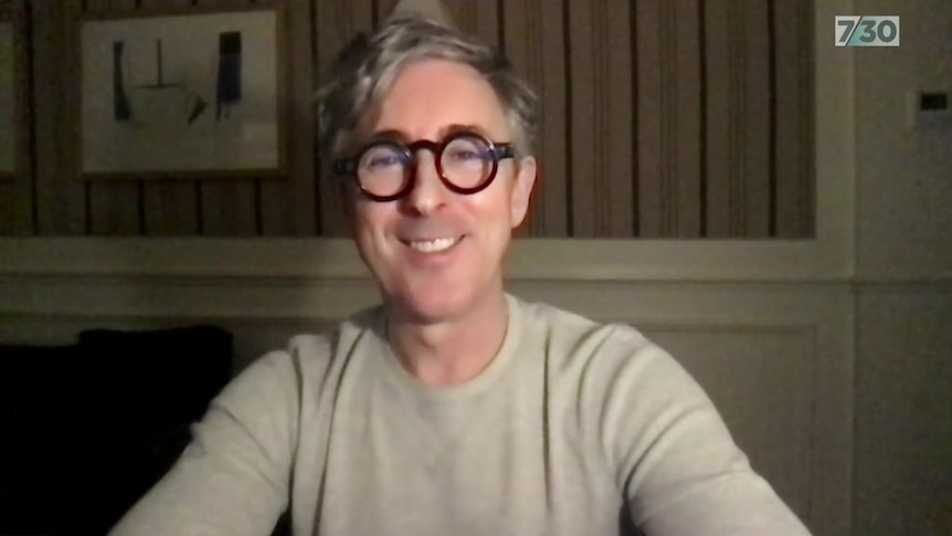 man in thick black circular spectacles smiling on zoom call