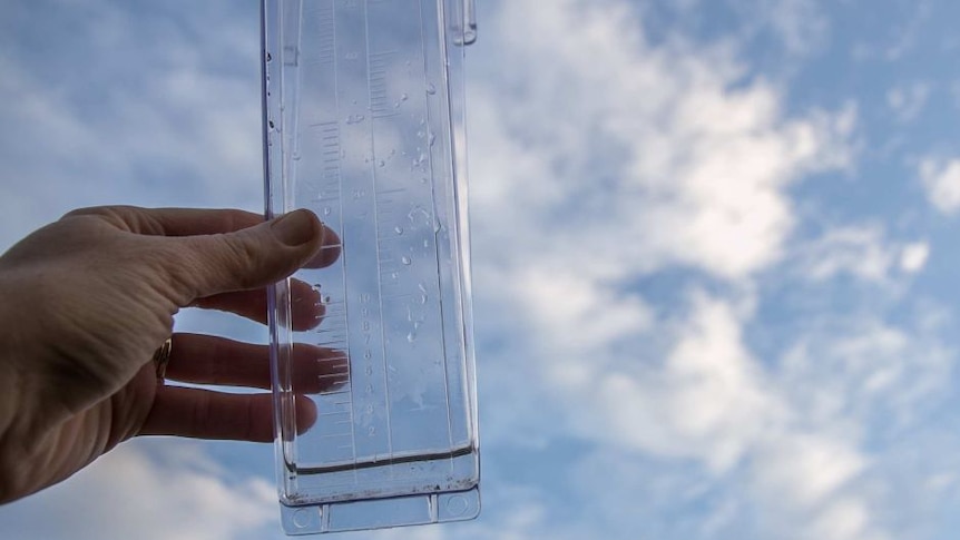 A hand holding a rain measurement gauge up to the sky.