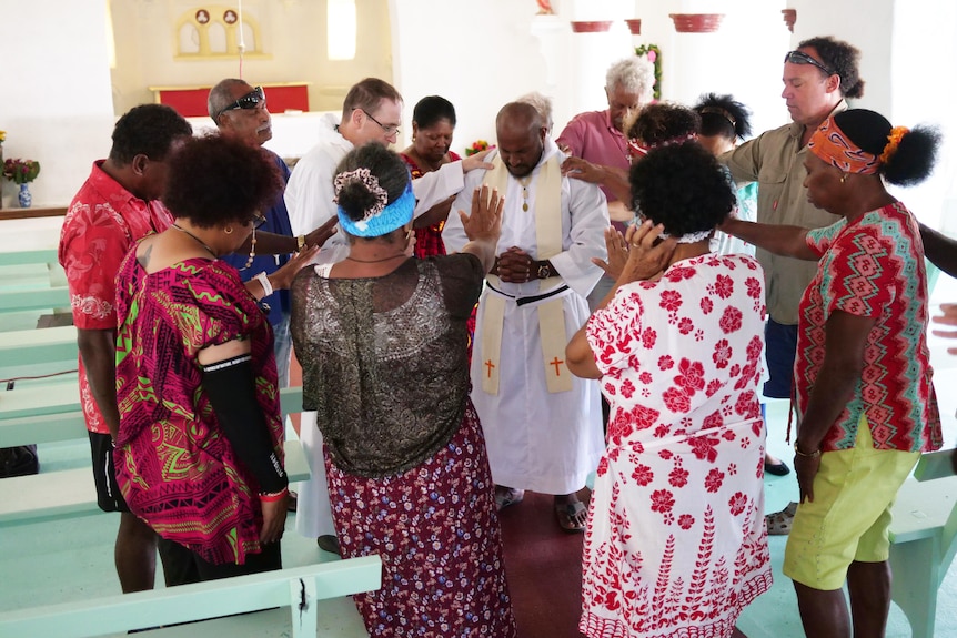 Anglican brother in the middle surrounded by people who have hands raised towards him. 