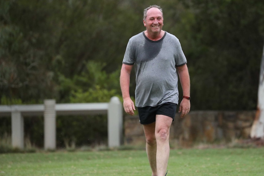Barnaby Joyce, smiling and sweaty, walks across a football field. He is wearing sports attire
