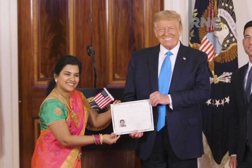 Donald Trump holds a certificate and American flag next to a woman in a sari