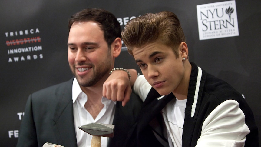 Scooter Braun stands next to Justin Bieber on a red carpet