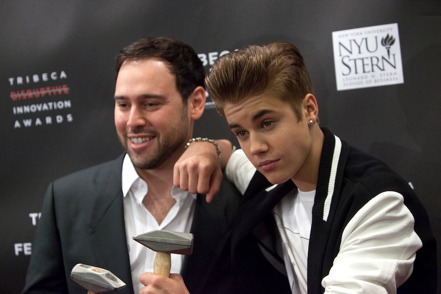 Scooter Braun stands next to Justin Bieber on a red carpet