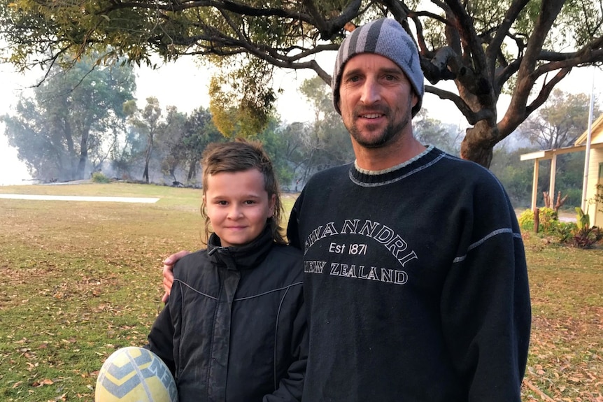 A boy holding a football stands next to a man.