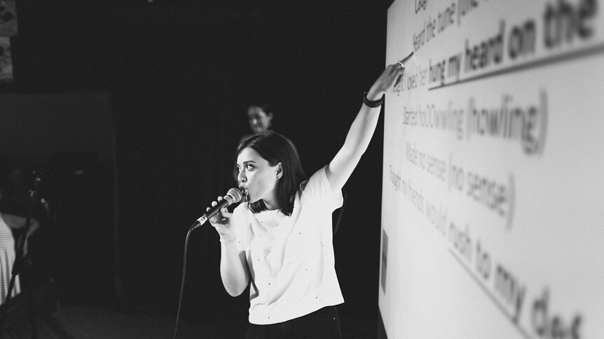 Woman stands against a projector screen which has the lyrics to a song.