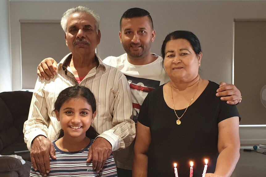 A family of four pose for photo together standing at a table with a cake on it with candles.