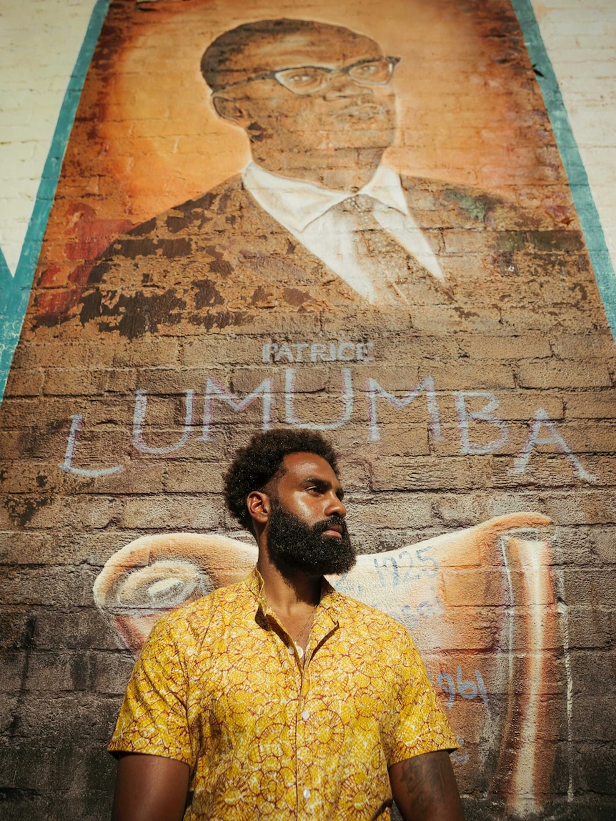 A man stands in front of a mural on a concrete wall.