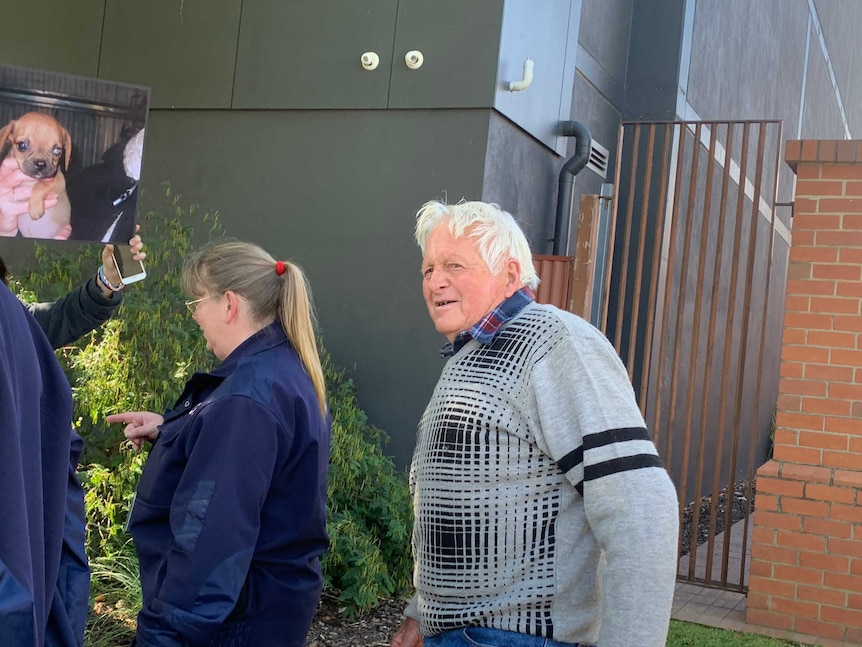 Bert Cooke walks out of the Sale Magistrates Court. A security guard stands between him and an animal activist holding a sign.