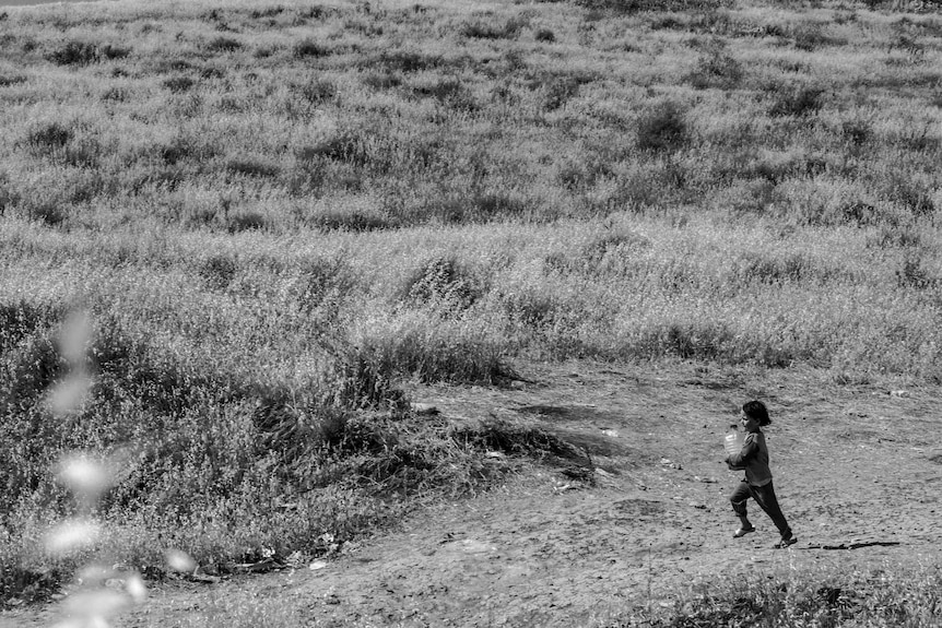 Small child runs across dry landscape clutching a water bottle