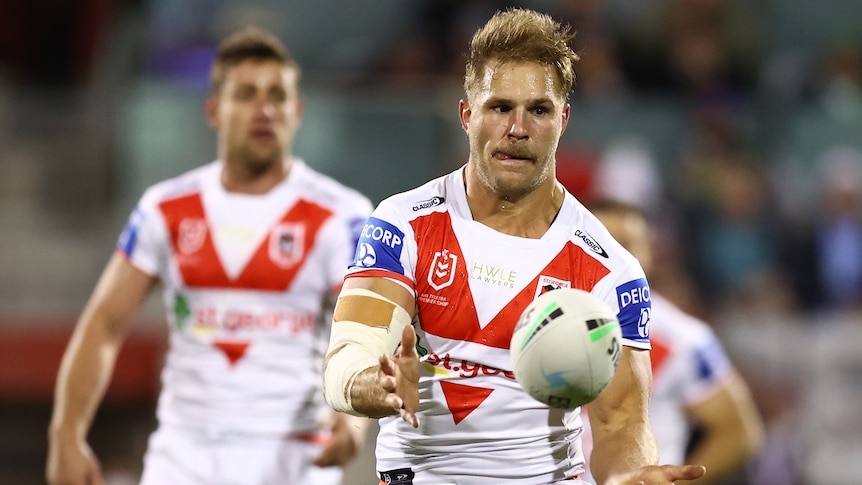 St George Illawarra Dragons player Jack de Belin passes a football. Teammate Andrew McCullough is blurred behind him.