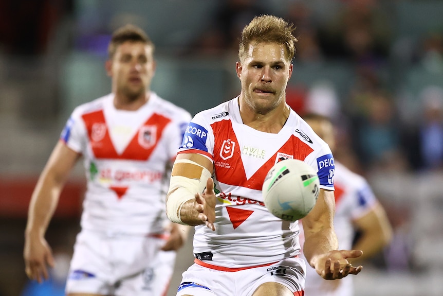 St George Illawarra Dragons player Jack de Belin passes a football. Teammate Andrew McCullough is blurred behind him.