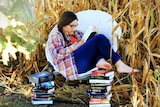 A woman with dark hair and wearing glasses sitting and reading in a field, to depict how fictional stories can change lives.