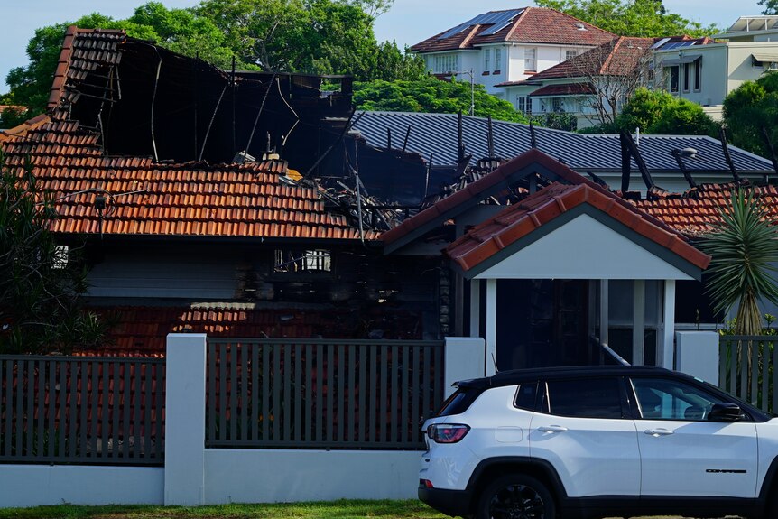 A house is blackened from fire, its roof partially destroyed