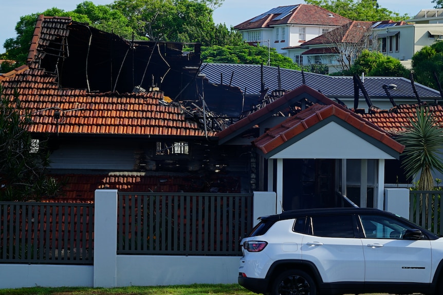 A house is blackened from fire, its roof partially destroyed