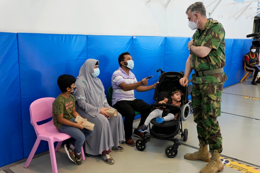 Um homem em exaustão militar fala com uma família de quatro pessoas