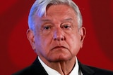 Mexico's President Andres Manuel Lopez Obrador stands on a stage with a red background