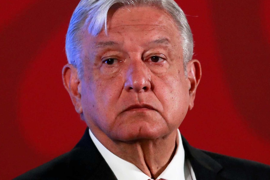 El presidente de México, Andrés Manuel López Obrador, se para en un escenario con un fondo rojo.