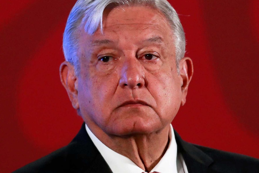 Mexico's President Andres Manuel Lopez Obrador stands on a stage with a red background