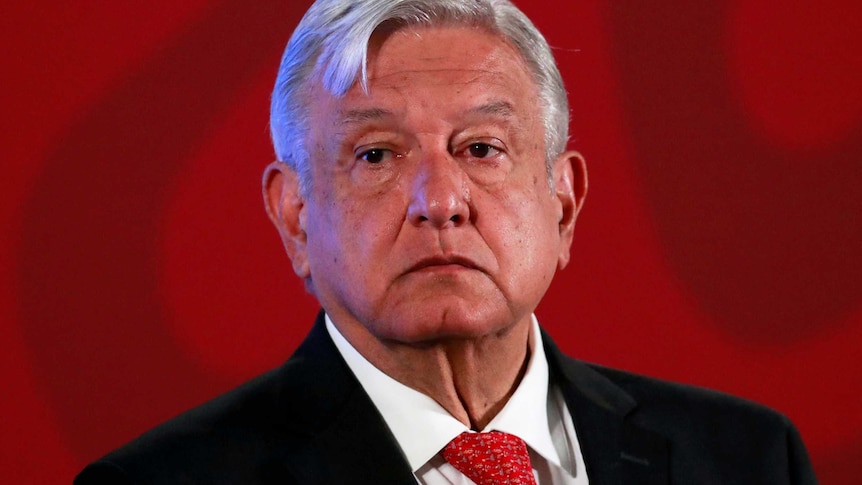 Mexico's President Andres Manuel Lopez Obrador stands on a stage with a red background