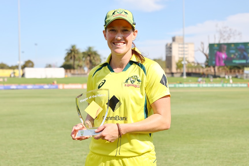 Megan Schutt stands in the sunshine at North Sydney Oval and smiles as she holds her glass POTM award