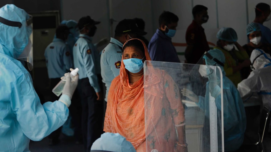 A woman wearing a face masks registers her details with a health worker in PPE