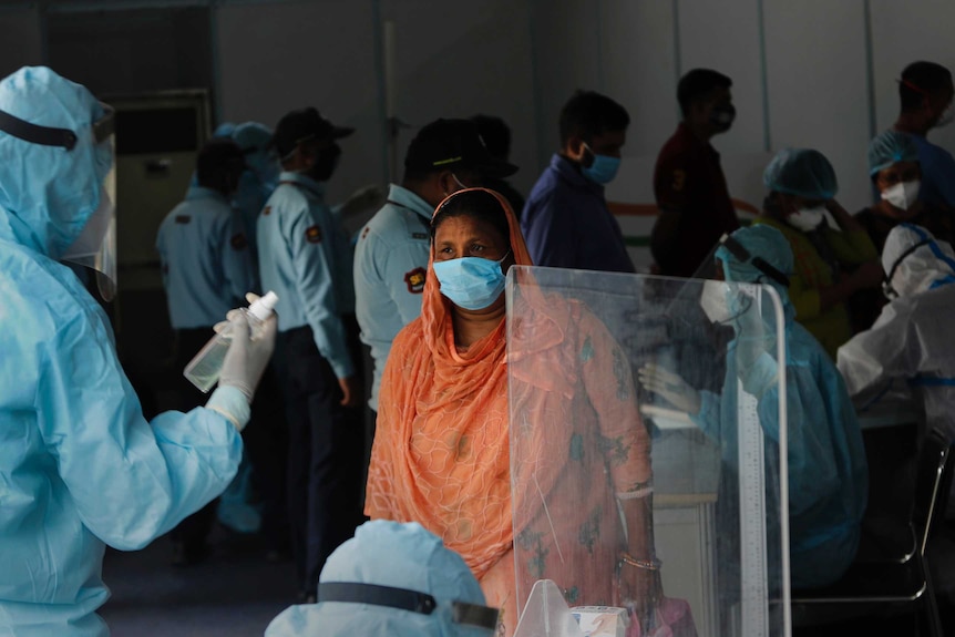 A woman wearing a face masks registers her details with a health worker in PPE