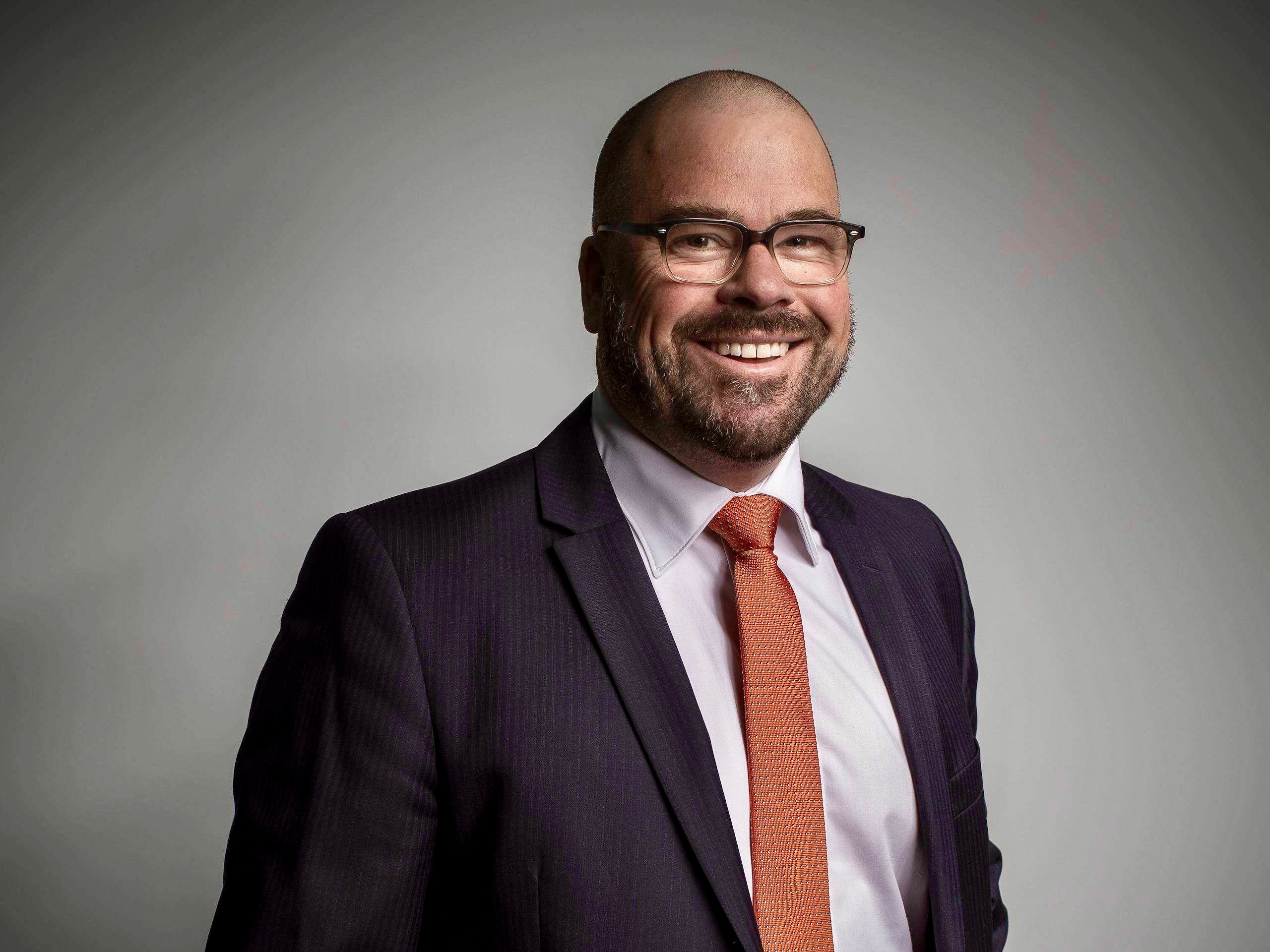 A man in a suit stands inside and smiles at the camera