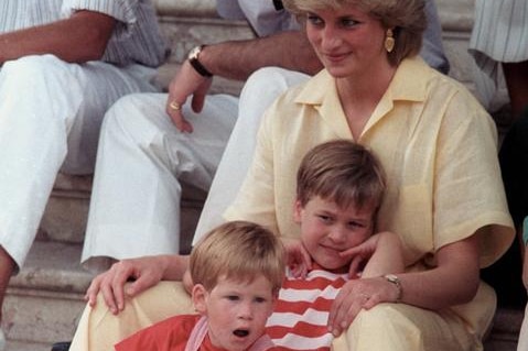 Princess Diana sits on the stairs in a yellow boiler suit with her sons on lower steps between her legs.