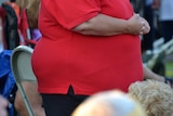 An overweight woman in a red shirt is seen standing at a social gathering.