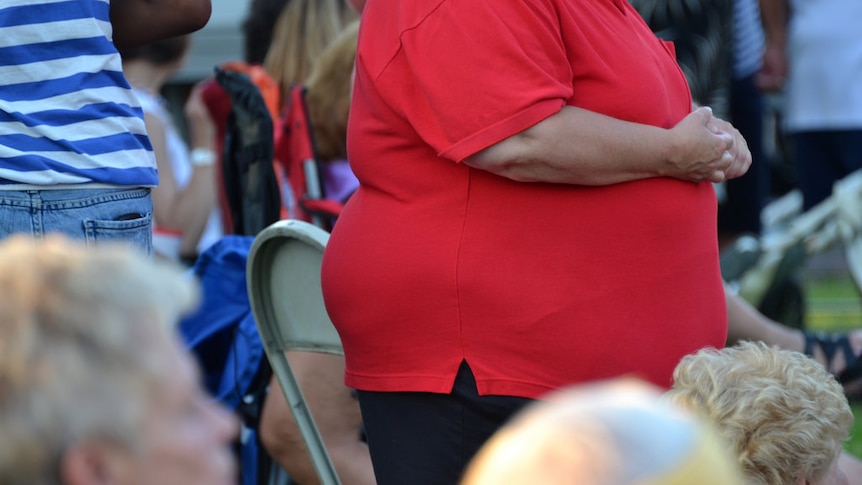 An overweight woman in a red shirt is seen standing at a social gathering.