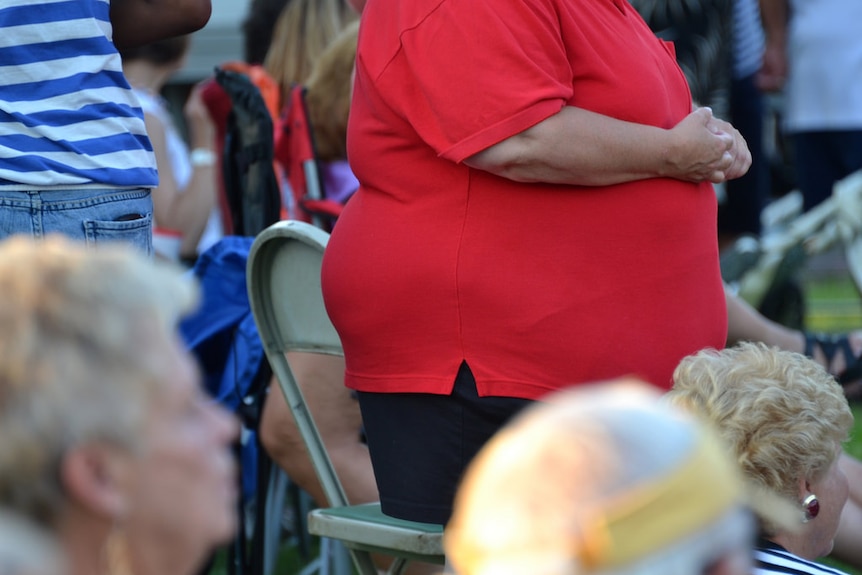 An overweight woman in a red shirt is seen standing at a social gathering.