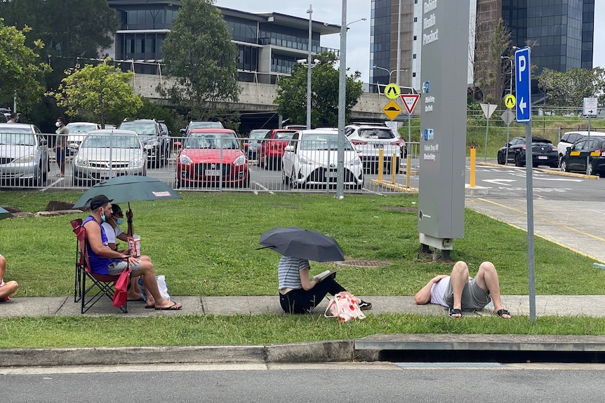 People lined up, some with umbrellas, some lying down on the footpath.