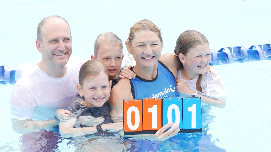 Michaela in the pool with her husband and three young kids holding a sign that says 101 on it