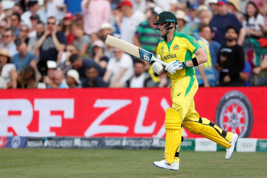 An Australian batsman runs out to bat, as people in the crowd cup their hands to boo him.