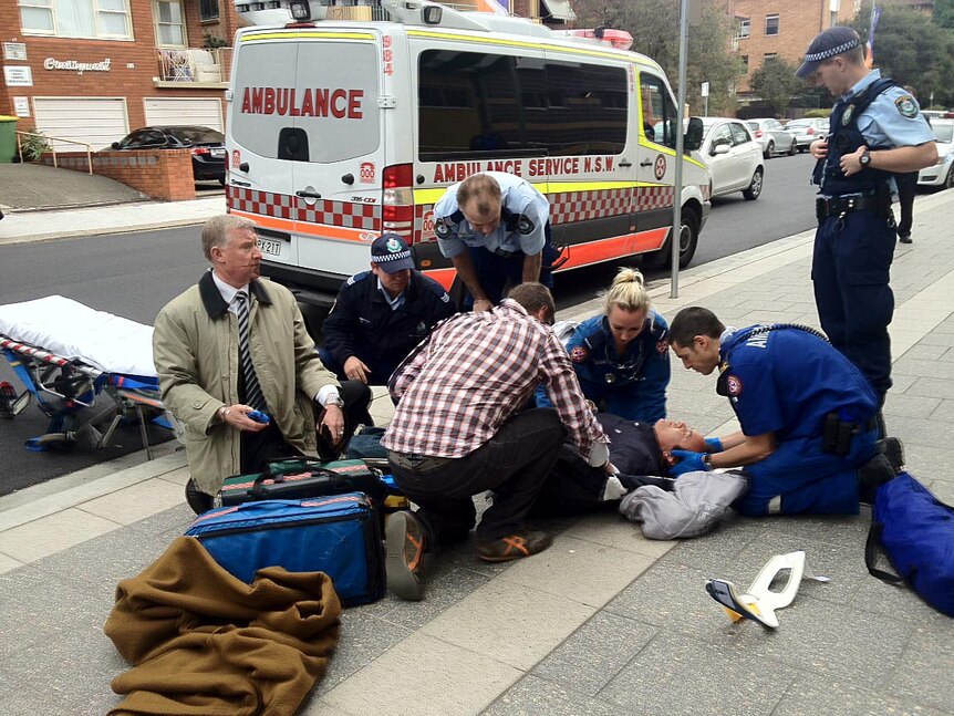 Paramedics tend to a Channel 9 cameraman on the ground outside court in Sydney.
